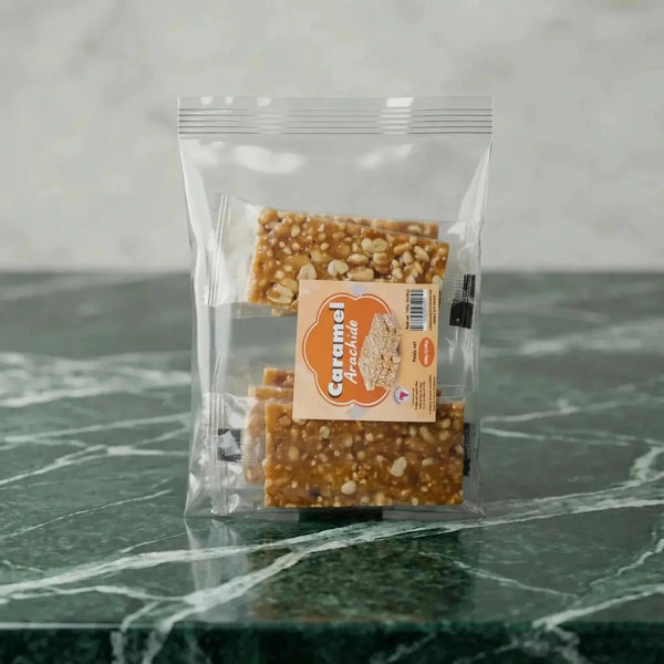 Barres de cacahuètes caramélisées "Caramel Arachide" en sachet transparent sur fond marbré vert.