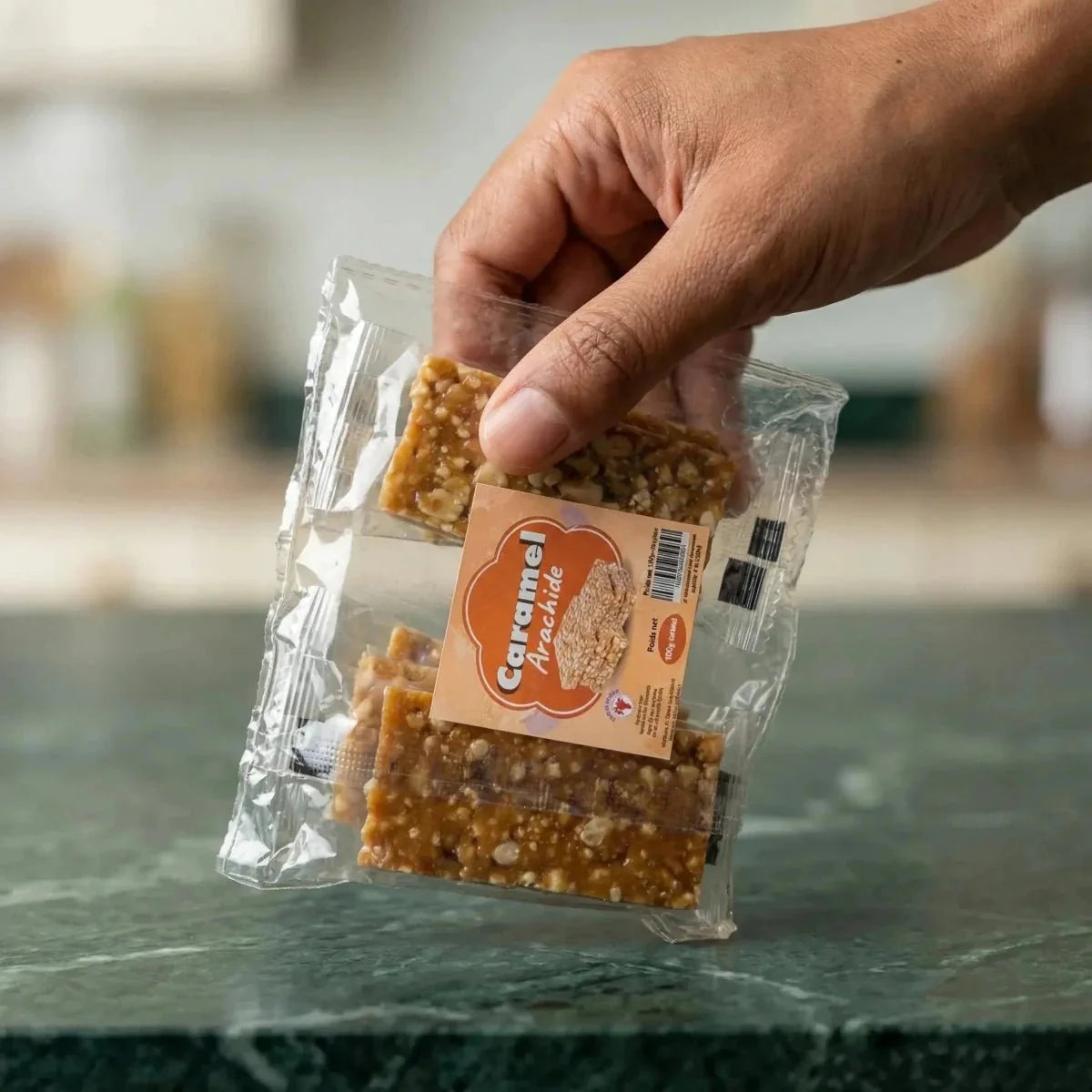 Barras de Maní con Caramelo Number One en bolsa de plástico, manos sosteniéndolas sobre fondo de cocina.