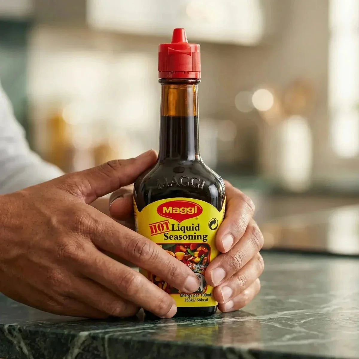Condimento liquido piccante Maggi, tenuto in mano su un bancone di marmo verde.