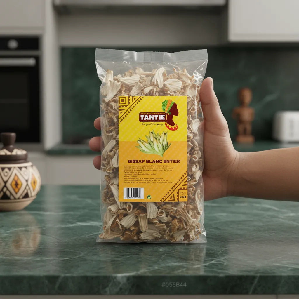 Main tenant un sachet de Bissap blanc entier TANTIE, plante séchée d’hibiscus pour infusions naturelles, sur fond de cuisine moderne.