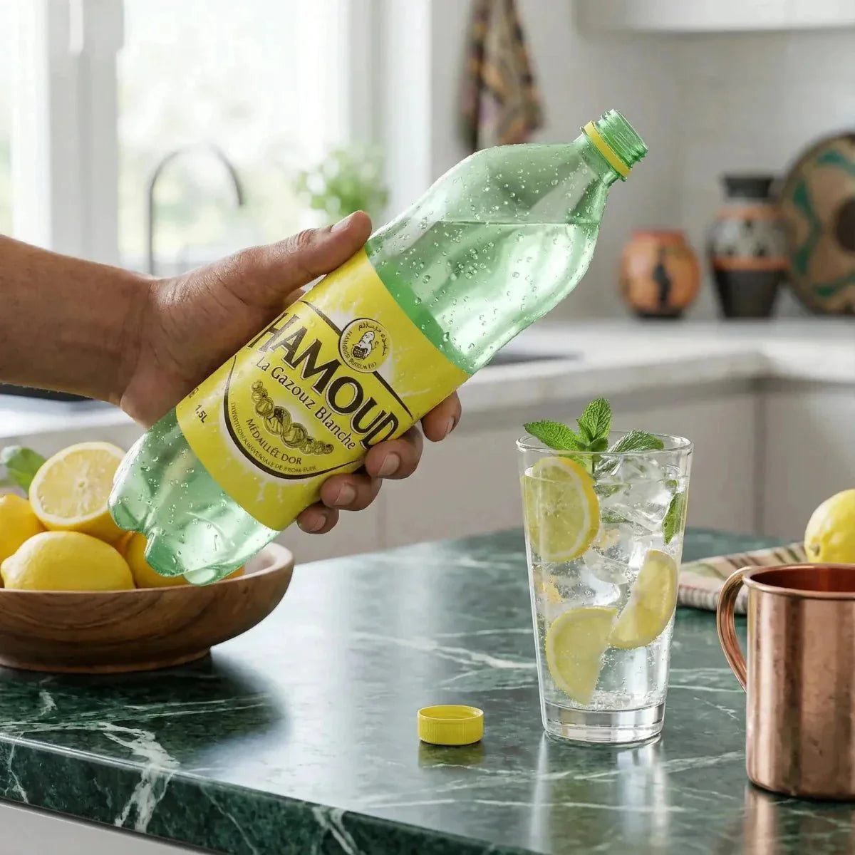 Fles 1,5L Hamoud limonade, hand schenkt in glas met citroen en ijs. Keukendecor.
