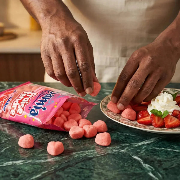 SAMIA zarte Erdbeerbonbons, offene rosa Tüte, dekoriert auf einem Teller mit frischen Erdbeeren.