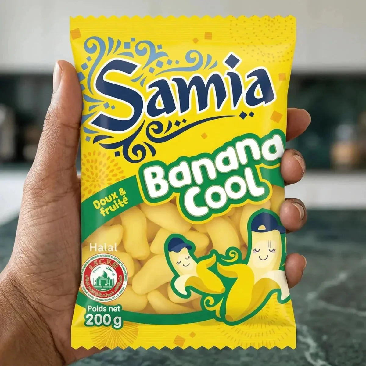 Caramelle alla banana halal Samia 200g, confezione gialla, scritte blu e verde, mano che tiene la bustina.