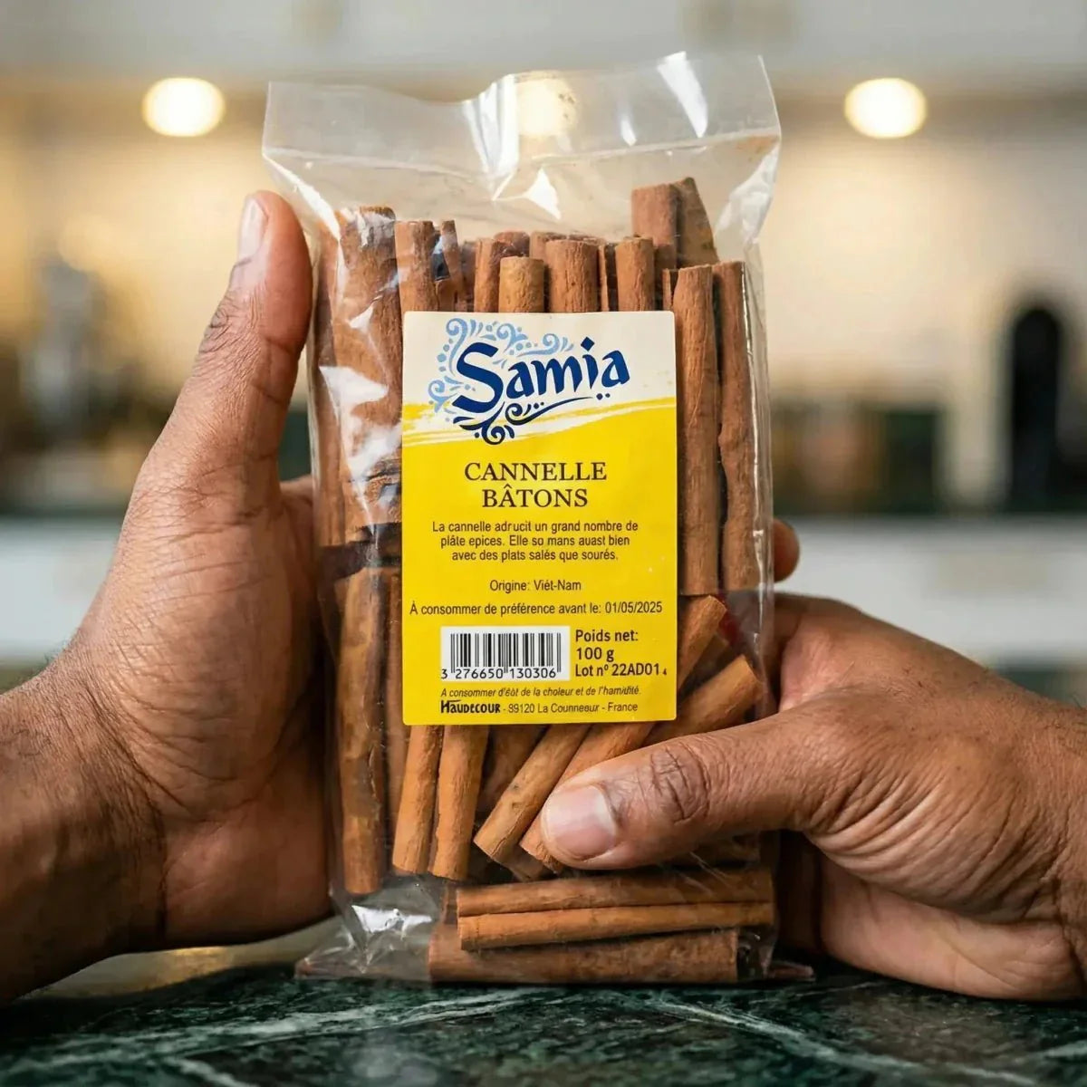 100g Samia cinnamon sticks packet, held in hands, on a green work surface.