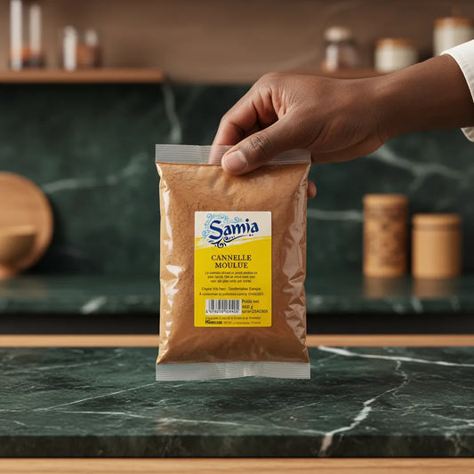 Main tenant un sachet de cannelle moulue SAMIA sur plan de travail - Cannelle Moulue Bio pour plats sucrés et salés.