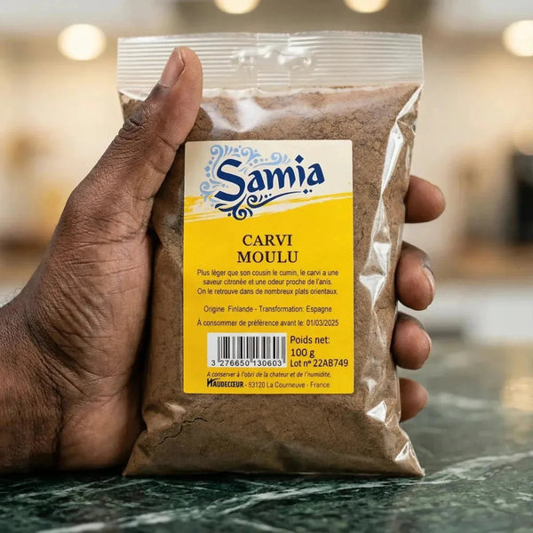 Eine 100g-Packung gemahlenen Kümmels von SAMIA, in der Hand gehalten, vor einem Marmorhintergrund.