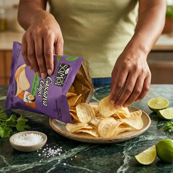 Chips de manioc SAMAI versées sur une assiette, mains en action. Citron vert et sel à côté.