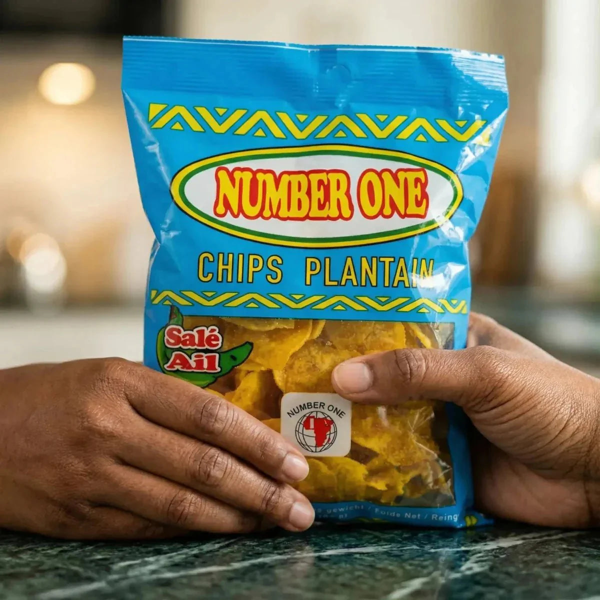 Blauwe zak met knoflook plantain bananenchips Nr. 1 vastgehouden door twee handen op een groene ondergrond.