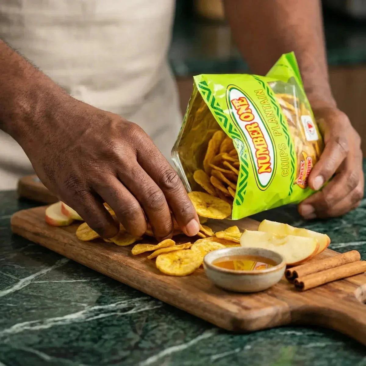 Plantainchips Nr. 1 en appels. Een zak chips uitgespreid op een plank met appels en honing.