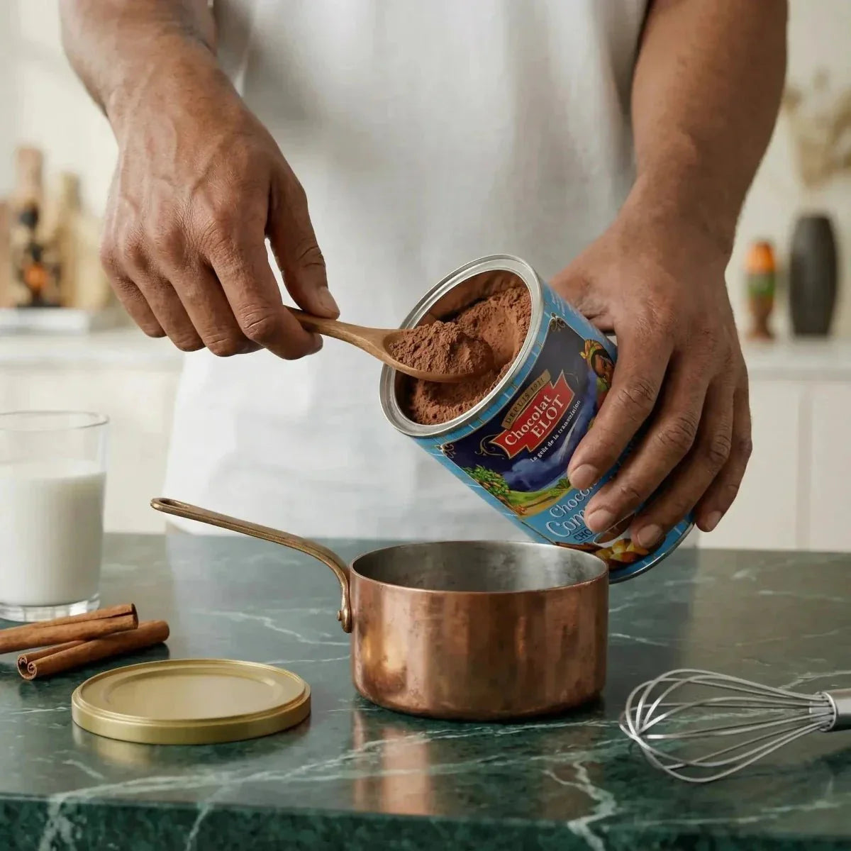 Communiechocolade ELOT gegoten in een steelpan. Pot cacaopoeder en houten lepel.