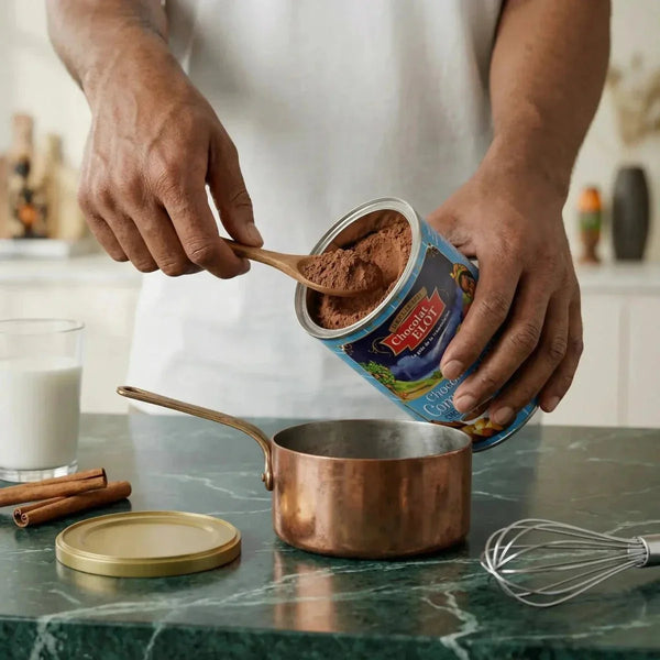 Chocolat de Communion ELOT versé dans une casserole. Pot de poudre de cacao et cuillère en bois.