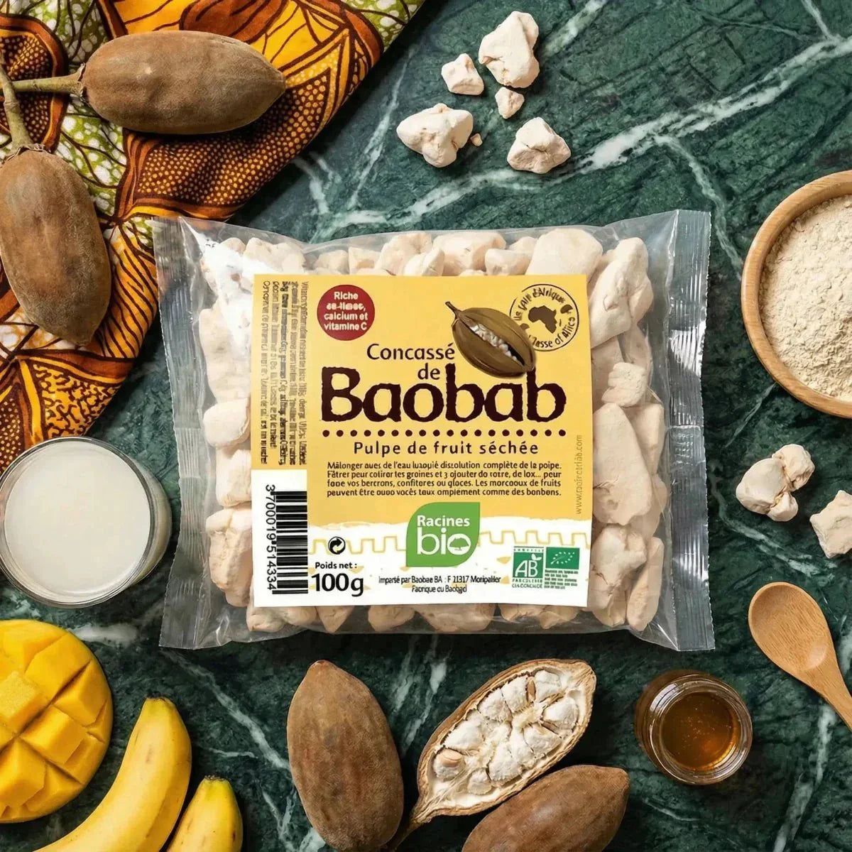 Concassé de baobab BIO RACINES, sachet 100g sur une table avec fruits frais, miel.