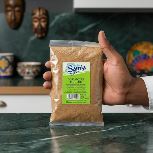 Main tenant un sachet de coriandre moulue SAMIA dans une cuisine décorée, épice fine idéale pour relever vos recettes maison.