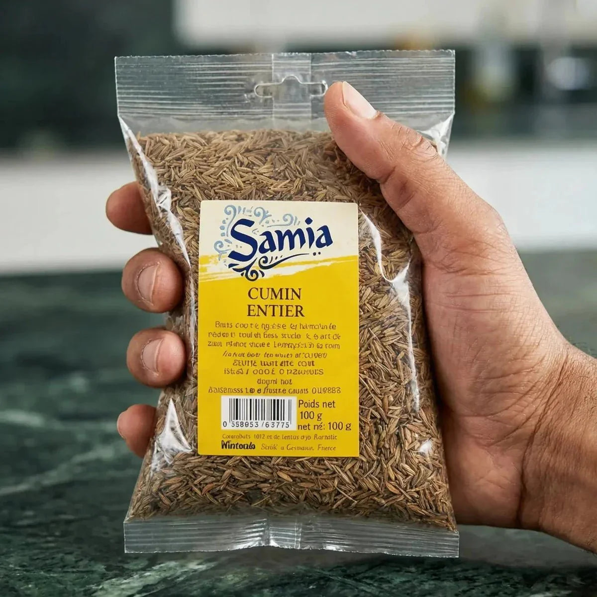 100g bag of whole Samia cumin held in a person's hand, close-up view.
