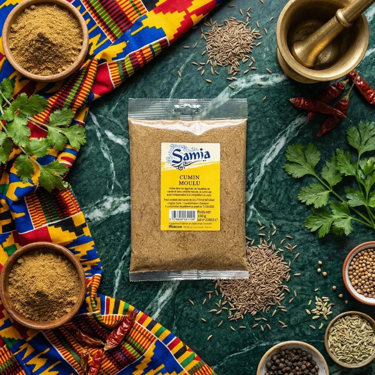 Cumin moulu SAMIA (100g) sur fond vert marbré, entouré d'épices, d'un tissu coloré.