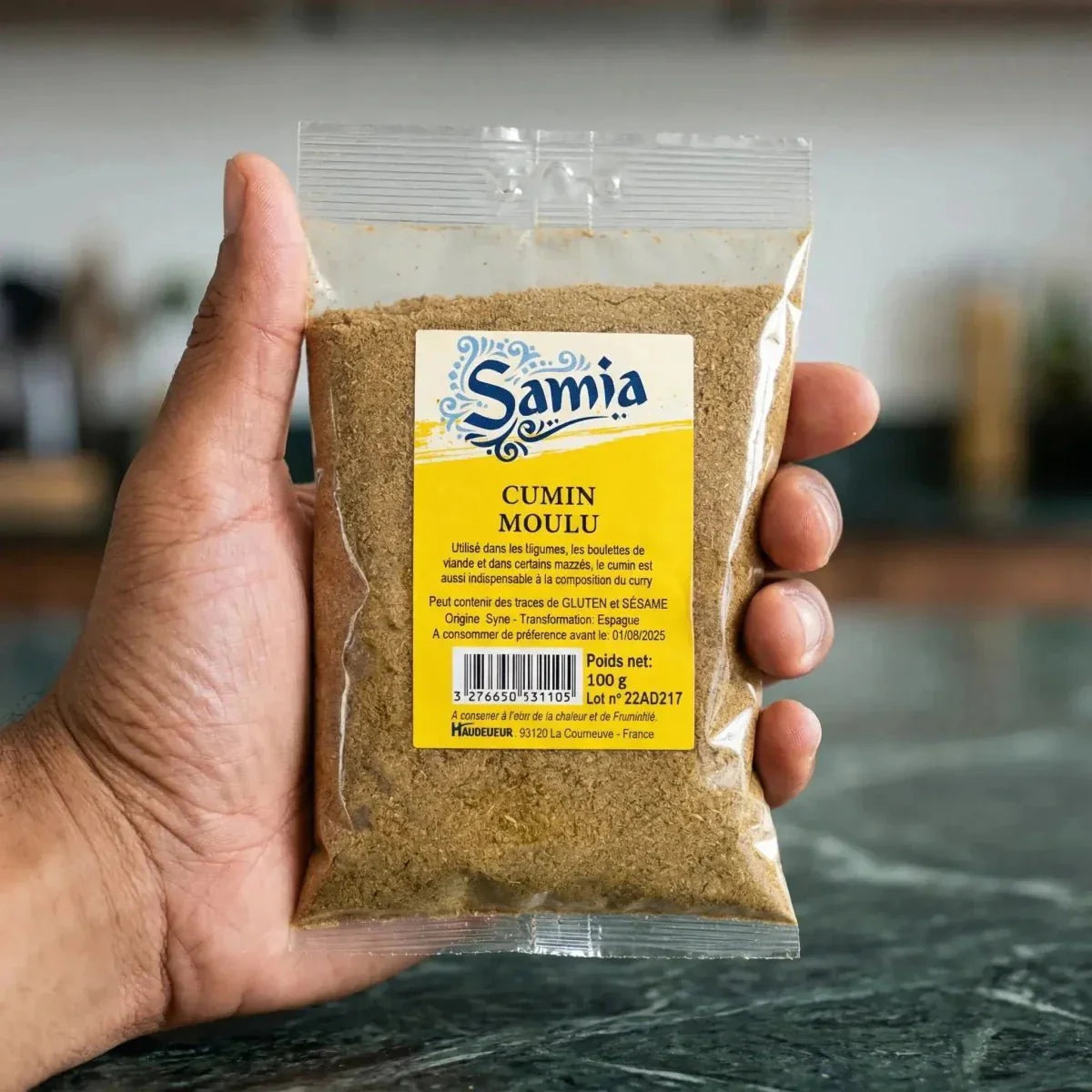 Sachet de cumin moulu SAMIA tenu à la main. On voit l'étiquette jaune et le produit à l'intérieur.