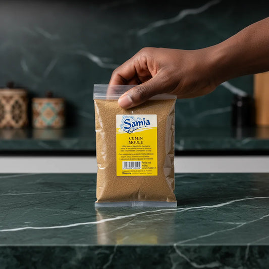 Main tenant un sachet de cumin moulu SAMIA sur plan de travail. Épice méditerranéenne incontournable pour l’assaisonnement des plats salés.