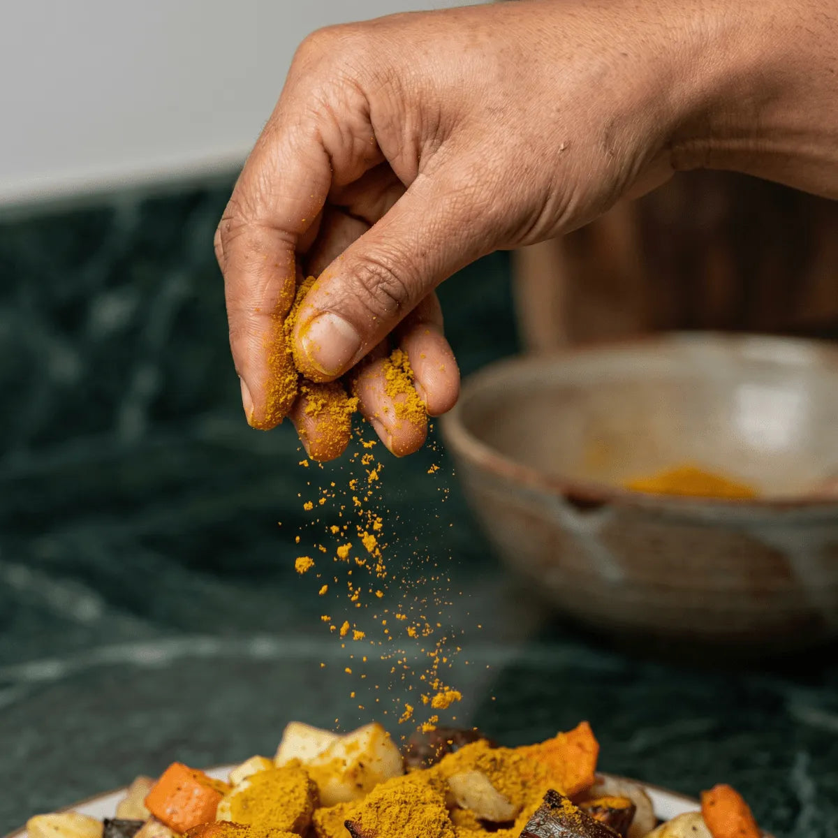 Curry madras SAMIA : Une main saupoudre d'épices un plat de légumes.