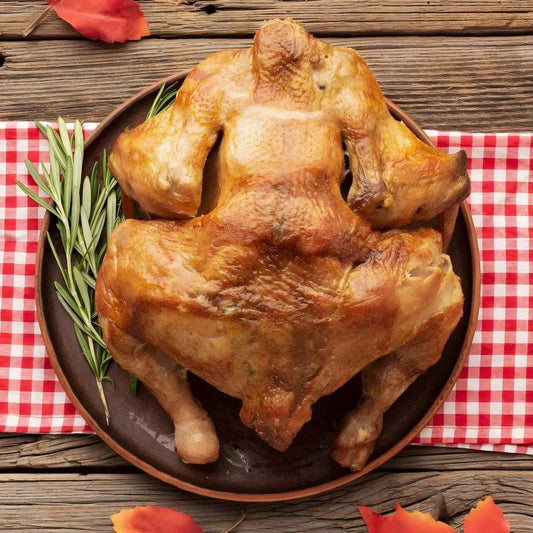 Coq fumé découpé servi sur assiette avec romarin, sur nappe à carreaux rouges, illustrant un produit de volaille prêt à consommer - VOLAILLE - NKOSI.