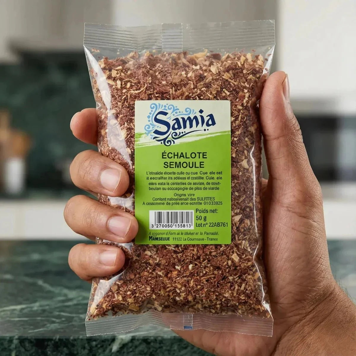 Sachet d'échalote semoule Samia présenté à la main, cuisine en arrière-plan.