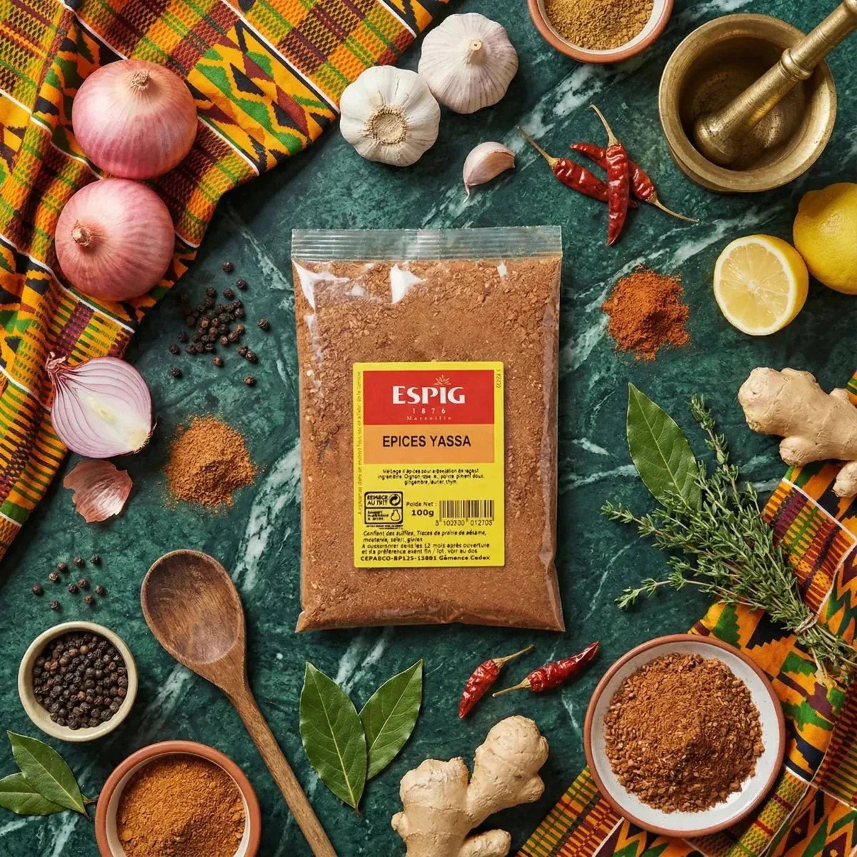 Yassa Spices ESPIG 100g. Culinary staging with fresh ingredients: onions, garlic, ginger.