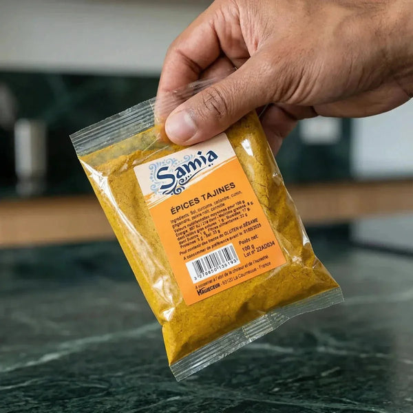 Sachet d'épices Tajines Samia tenu à la main, sur un plan de travail vert sombre.
