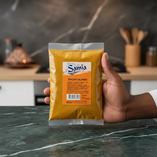 Main tenant un sachet d'épices pour tajine SAMIA 100g, mélange d'épices pour plats mijotés, idéal pour recettes marocaines et orientales.