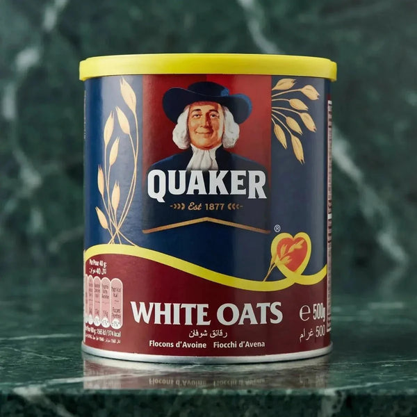 Boîte de flocons d'avoine Quaker White Oats sur un fond marbré. L'emballage est rouge, bleu, jaune.