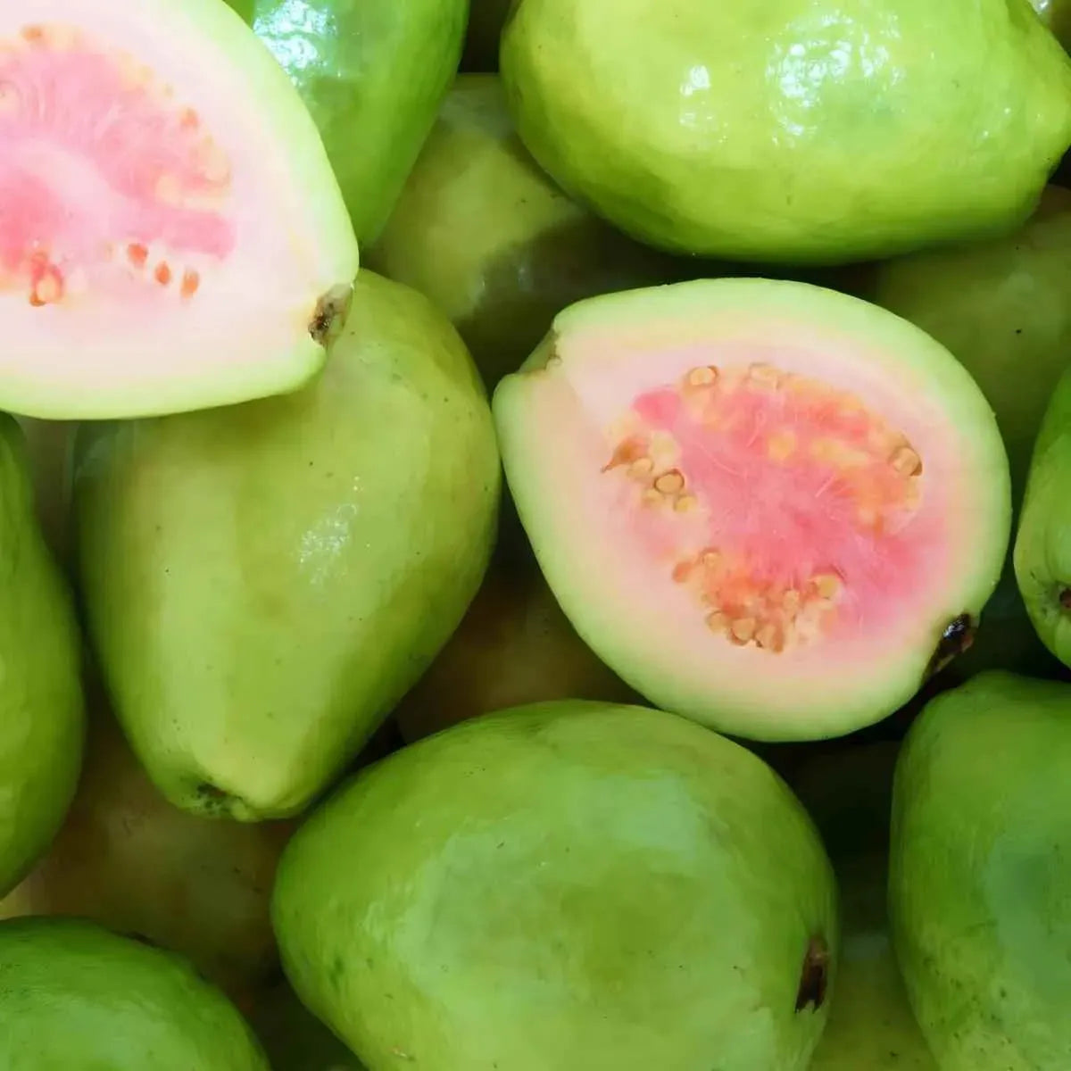 Goyaves roses entières et coupées exposant leur chair rose, fruit tropical frais idéal pour jus, desserts et salades.