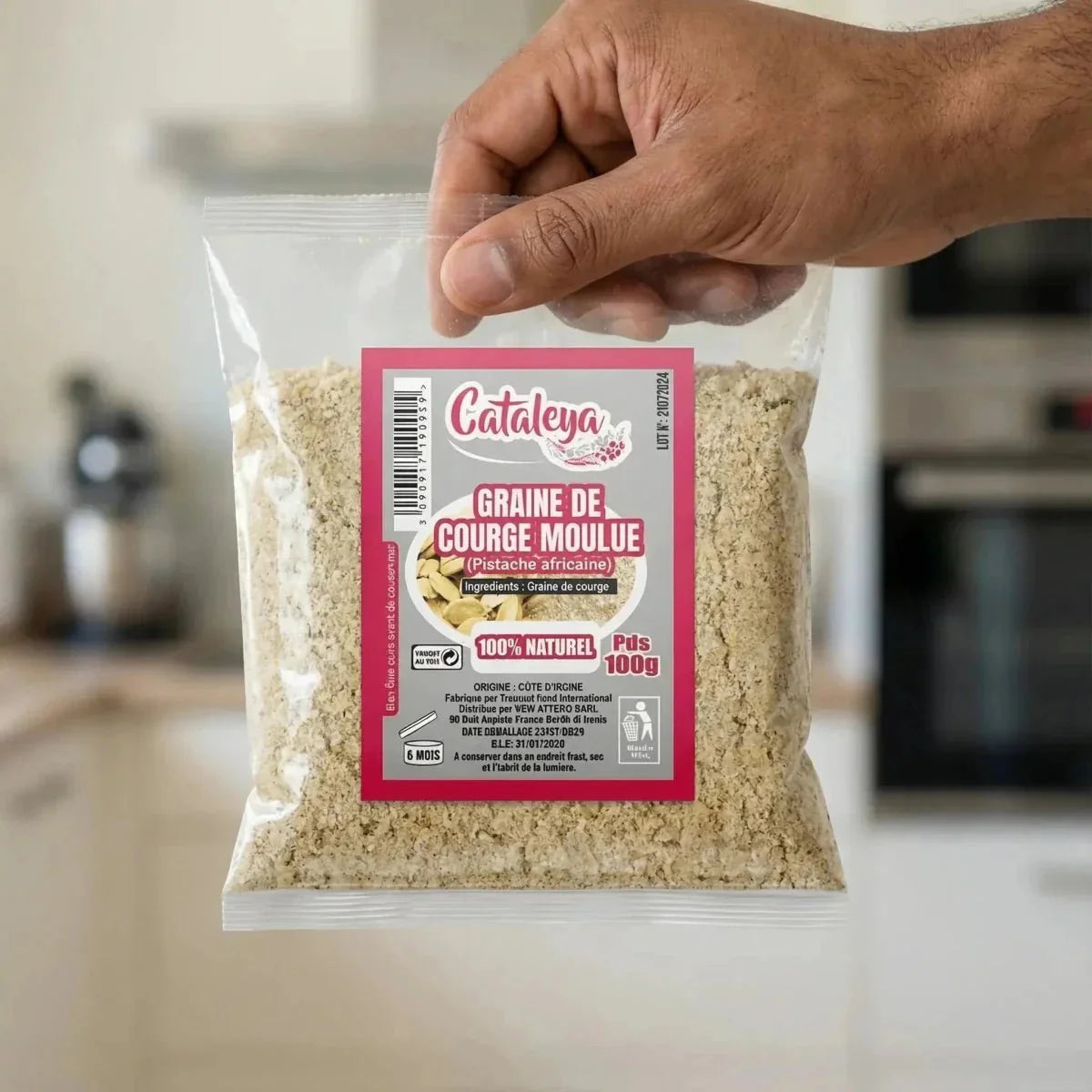 Paket gemahlener Kürbiskerne CATALEYA, gehalten von einer Hand, vor einer unscharfen Küche.