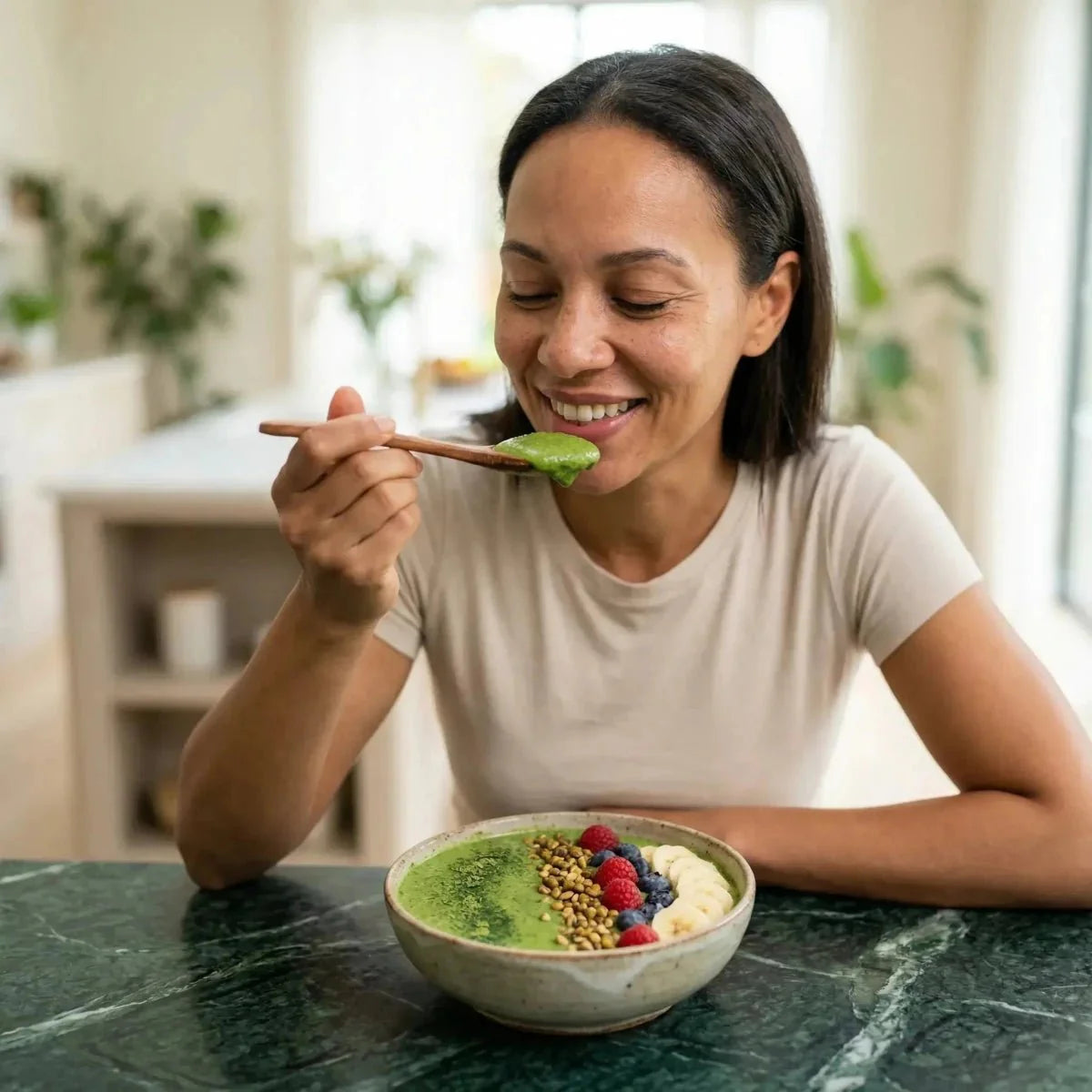 NUMBER ONE Moringazaad. Lachende vrouw eet een groene smoothie bowl met fruit.