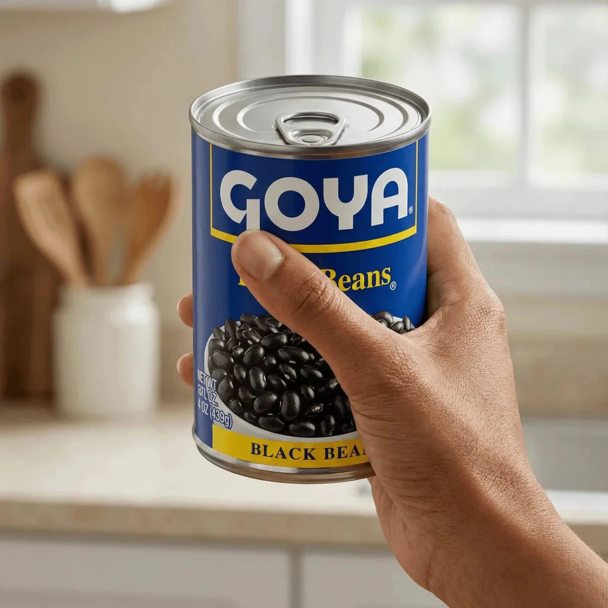 Can of black beans by GOYA, held in one hand, in front of a blurred kitchen background.