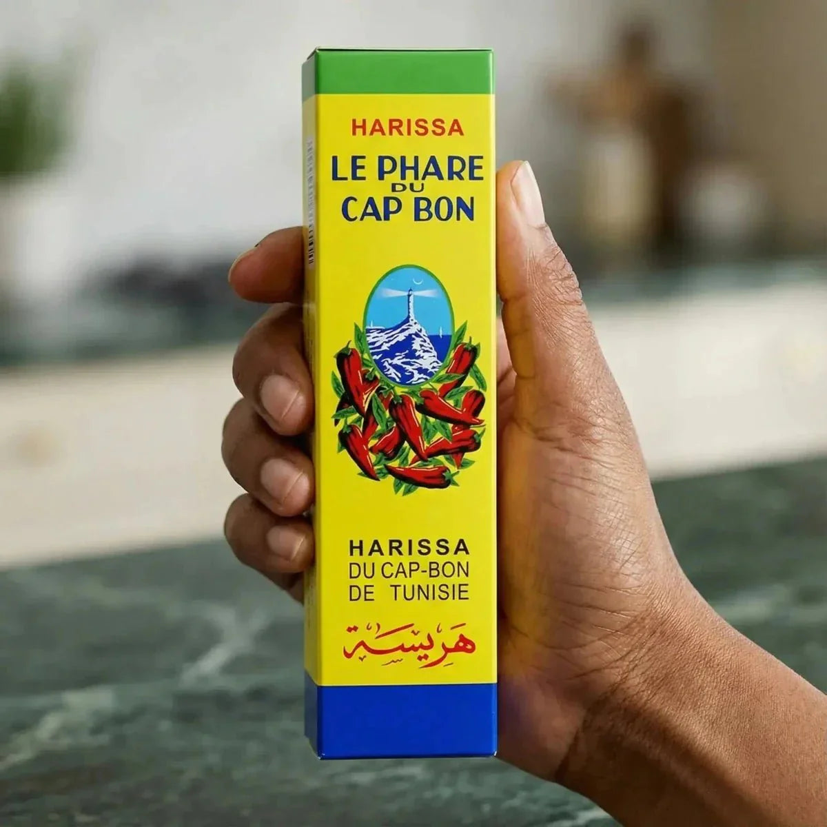 Tube de Harissa Le Phare du Cap Bon, tenu en main. Emballage jaune, vert et bleu.