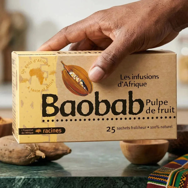 Boîte d'infusion d'Afrique au baobab RACINES tenue par une main, avec fruits de baobab.