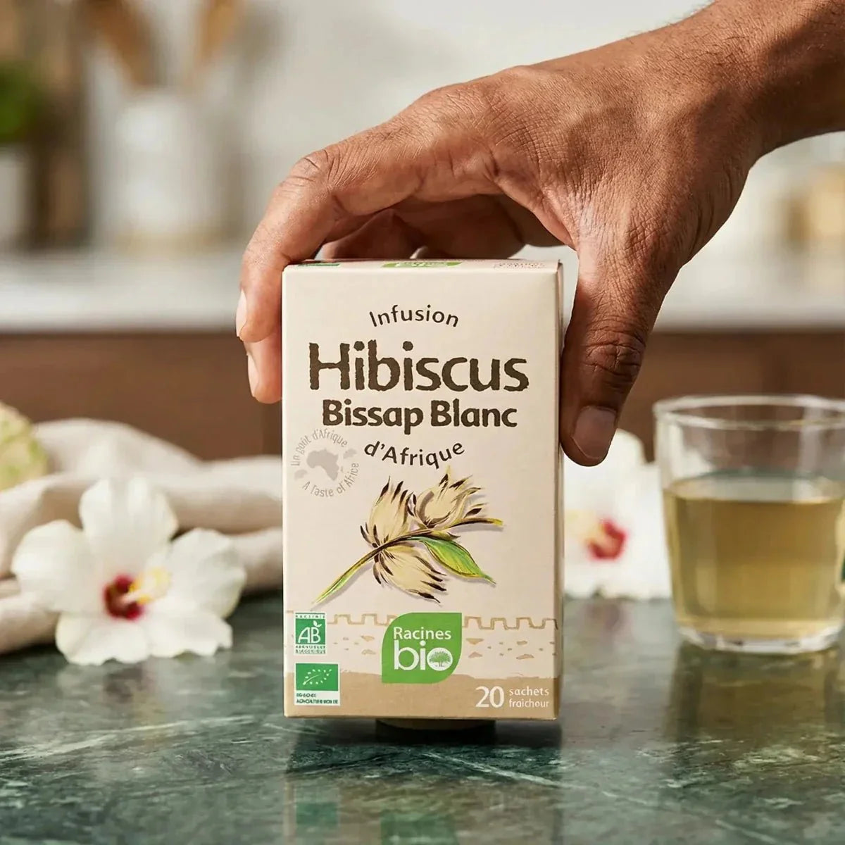 Infusion hibiscus blanc bio, de Racines Bio, dans son emballage, avec une tasse de thé à côté.