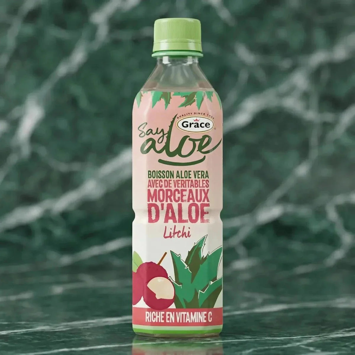 Aloëveradrank met lychee van Grace, met stukjes aloë, op een groen marmeren achtergrond.