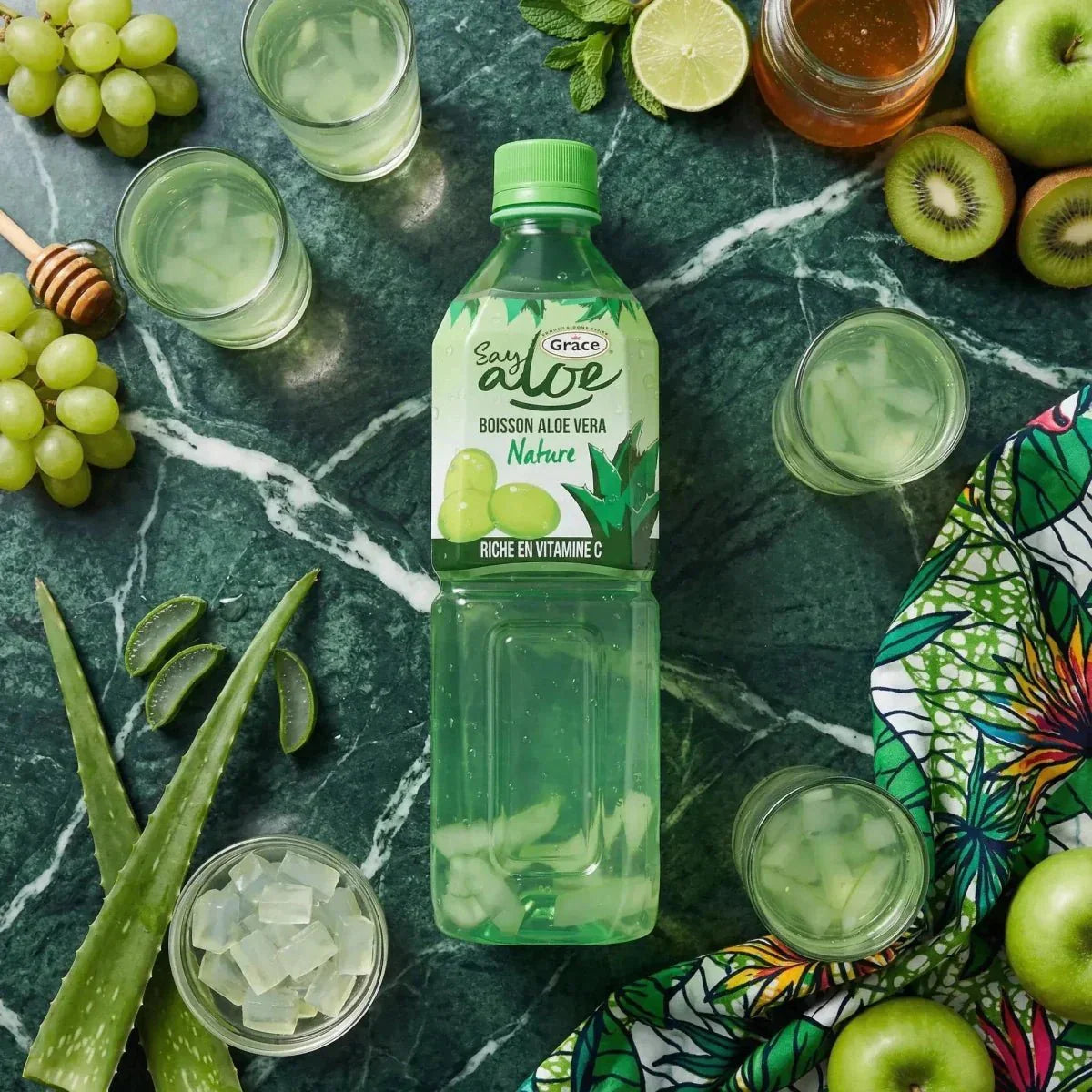 Jus d'Aloe vera GRACE 1L sur fond vert marbré avec raisins, pommes, kiwi, aloe vera.