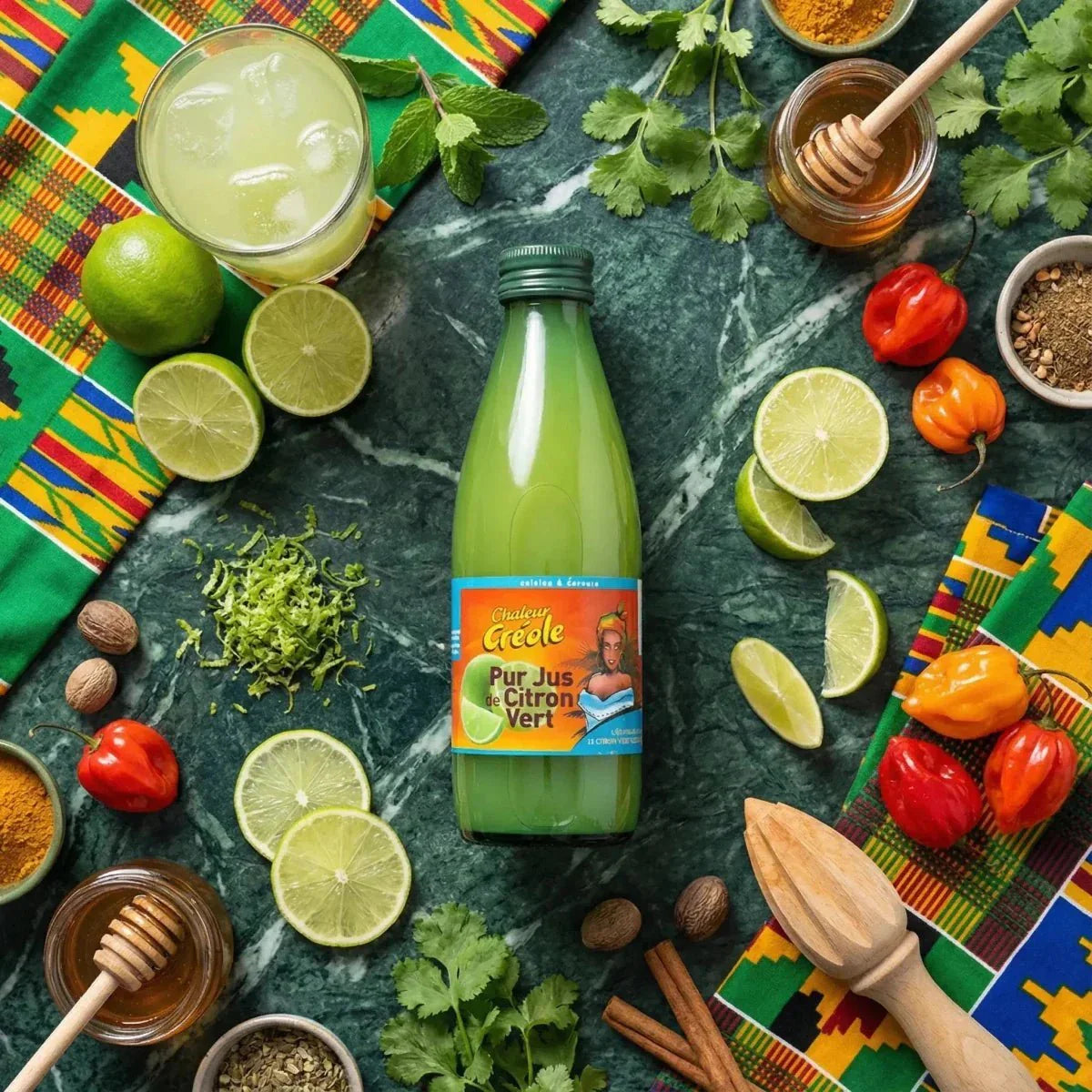 Lime juice CHALEUR CRÉOLE, 25mL. Bottle and glass surrounded by limes, chili peppers, honey.