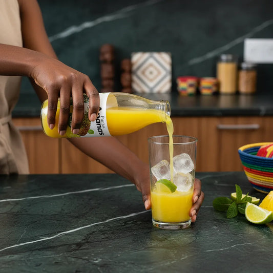 Versement de Pur jus Ananas RACINES BIO dans un verre avec glaçons et citron vert, boisson rafraîchissante bio sans sucre ajouté.