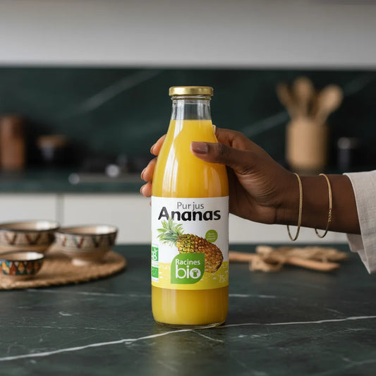 Main tenant une bouteille de Pur jus Ananas RACINES BIO sur un plan de travail, boisson bio sans sucre ajouté, idéale pour une consommation quotidienne.
