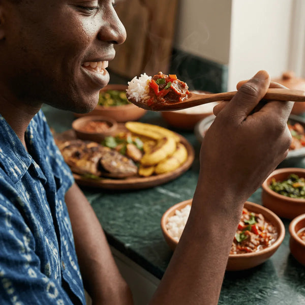 Un homme goûte une cuillerée de riz blanc et de sauce tomate épicée, avec des bananes plantain frites sur la table