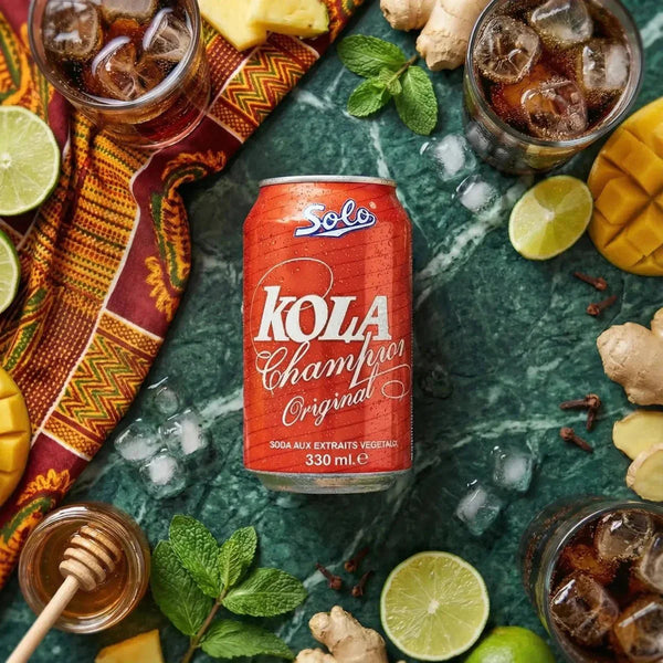 Kola Champion SOLO 330ml vor grün marmoriertem Hintergrund, umgeben von Limette, Mango, Ingwer, Honig.