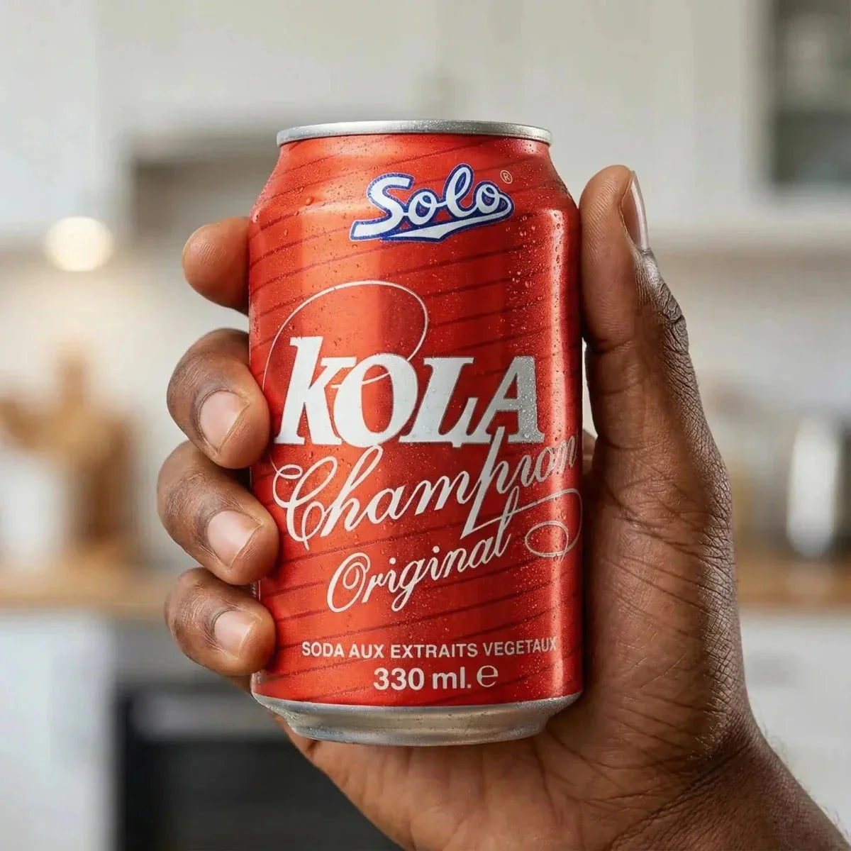 Champion SOLO Kola Can 330mL held by a hand. Refreshing drink against a kitchen background.