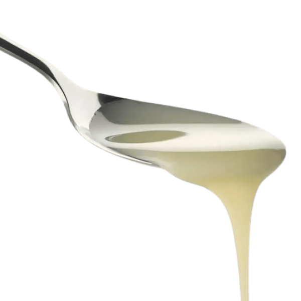 Lait concentré non sucré versé d'une cuillère, avec des reflets brillants.
