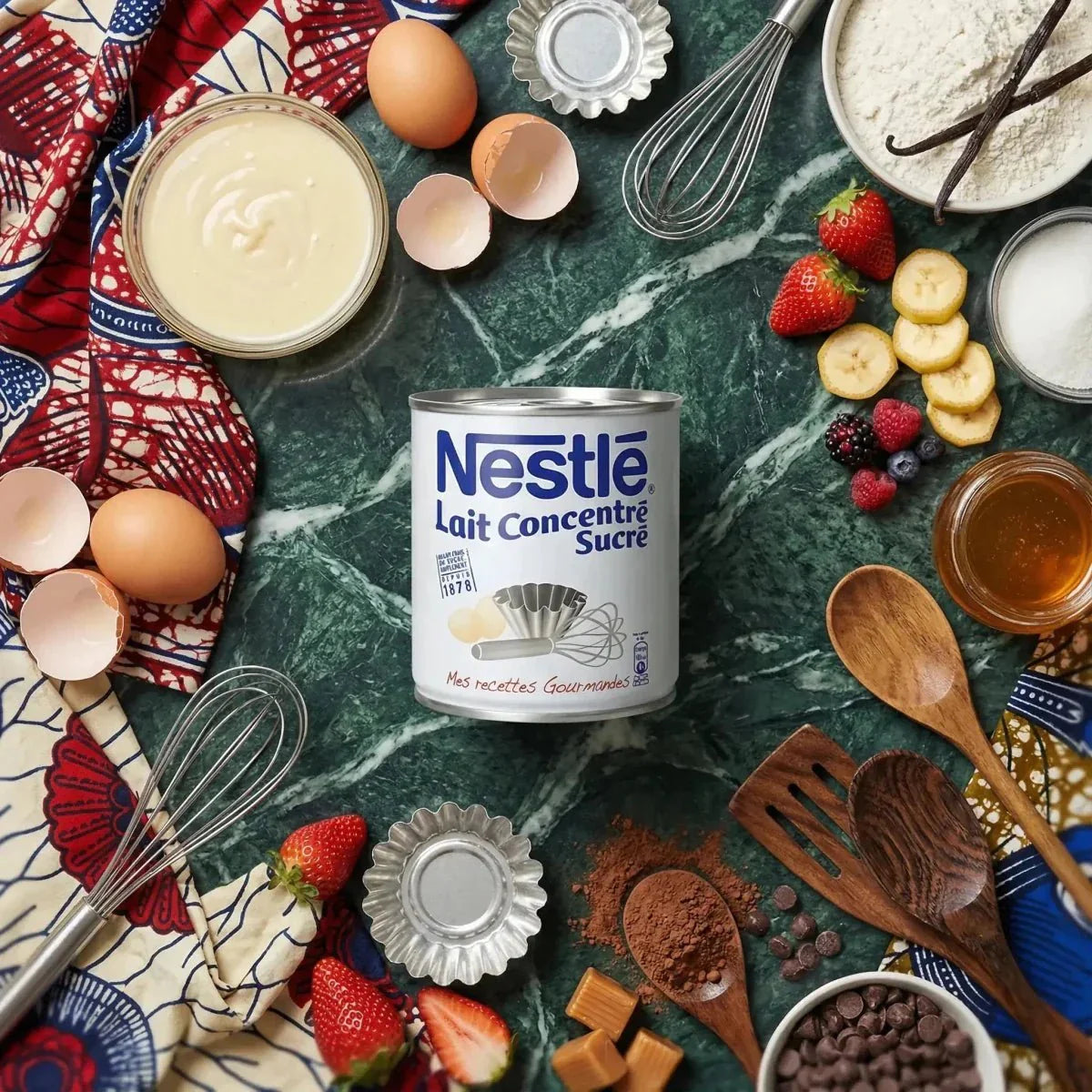 Boîte de lait concentré sucré Nestlé entourée d'ingrédients et d'ustensiles de cuisine vert marbré.