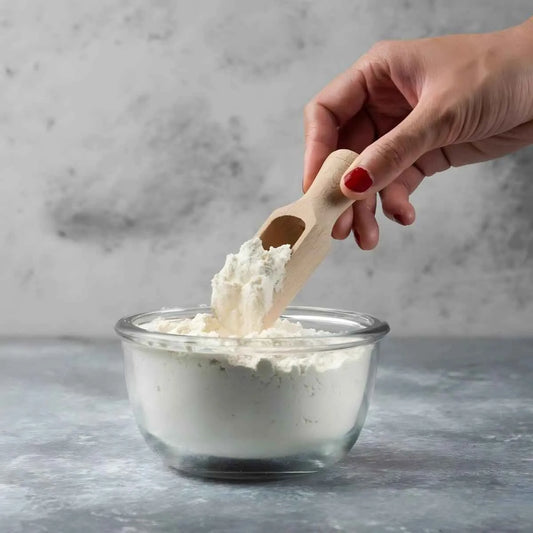 Lait en poudre NIDO dans un bol en verre avec cuillère en bois, parfait pour la cuisine et les préparations laitières riches en calcium et protéines.