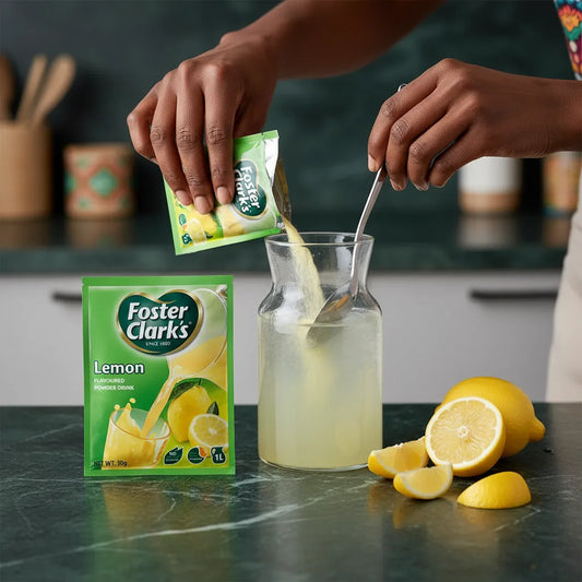 Préparation du jus en poudre citron FOSTER CLARKS dans une carafe avec eau et citrons frais, boisson instantanée au goût fruité et acidulé.