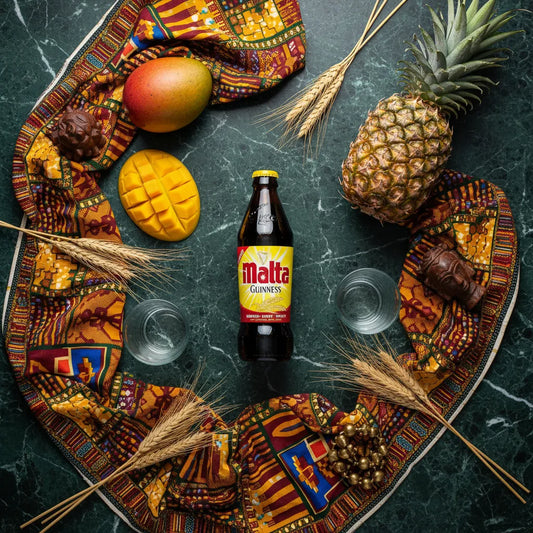 Bouteille de boisson au malt GUINNESS entourée de fruits tropicaux et d’éléments culturels africains, illustrant son goût exotique et unique.
