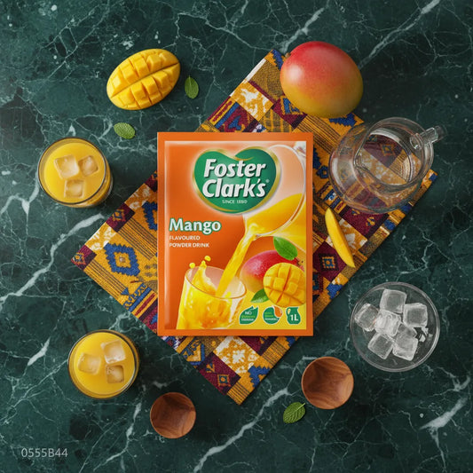 Sachet de Jus Mangue en Poudre - FOSTER CLARKS posé sur une nappe colorée avec mangues fraîches, glaçons et verres de jus.