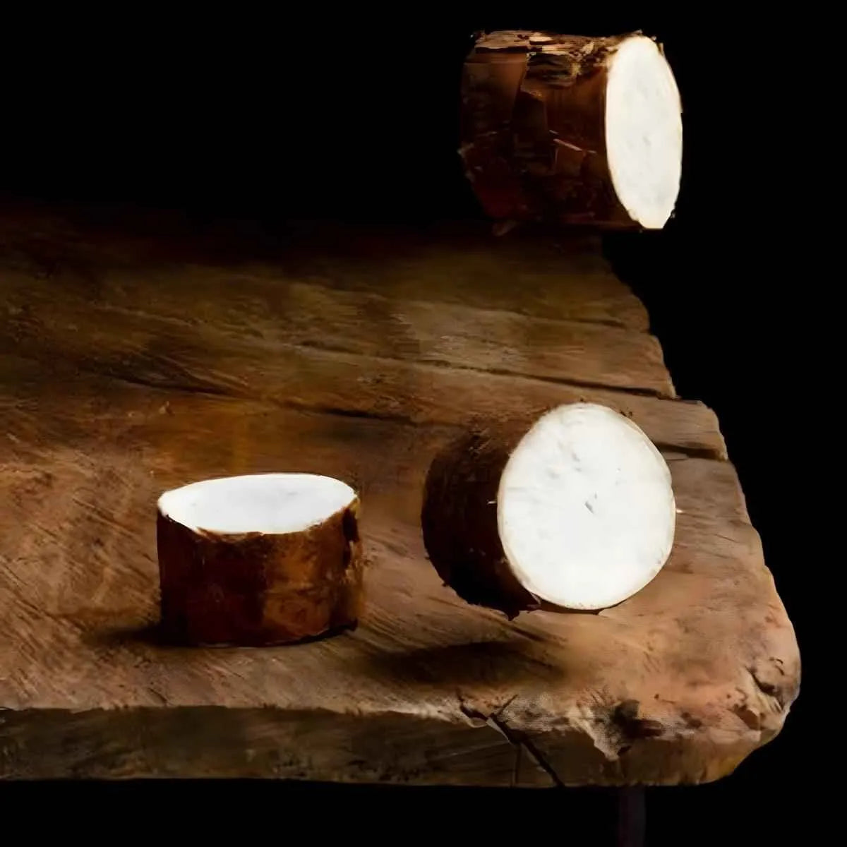 Tronçons de manioc frais non épluchés sur table rustique, illustrant l'aspect brut du manioc avant surgélation et découpe.